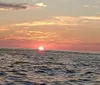 The image captures a serene sunset over the ocean with the sun hanging low on the horizon casting a warm glow across the sky and water