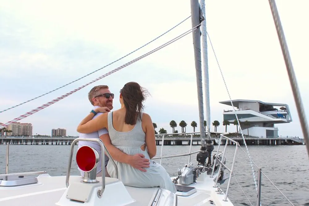 Two people are enjoying a moment together on a sailboat with a coastal cityscape in the background