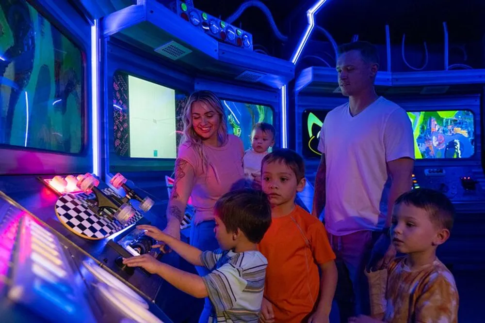 A family with three children is playing arcade games together in a vibrant neon-lit gaming room