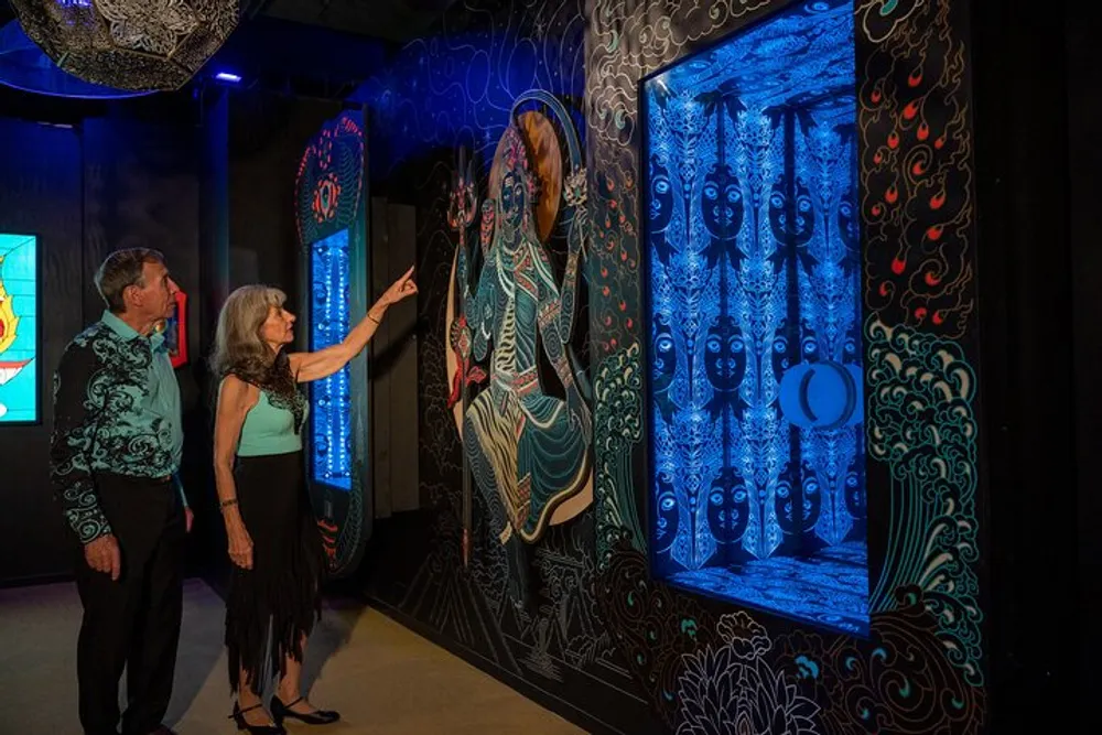 Two people are observing and pointing at a colorful illuminated wall art display inside a gallery-like setting