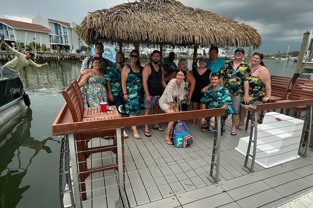 A group of people are posing for a photo on a dockside tiki bar with a thatched roof exuding a relaxed tropical atmosphere