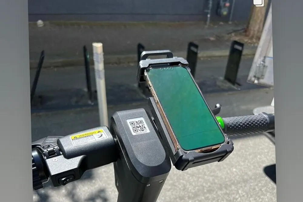 An electric scooters handlebar is equipped with a phone mount holding a smartphone with a green screen