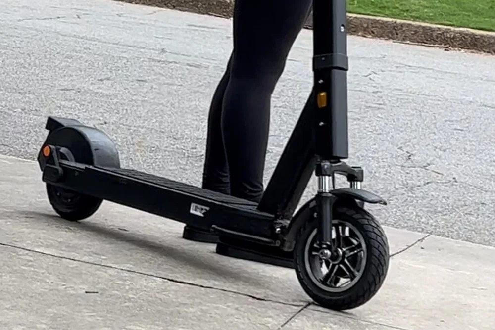 A person is standing on an electric scooter thats parked on a concrete sidewalk