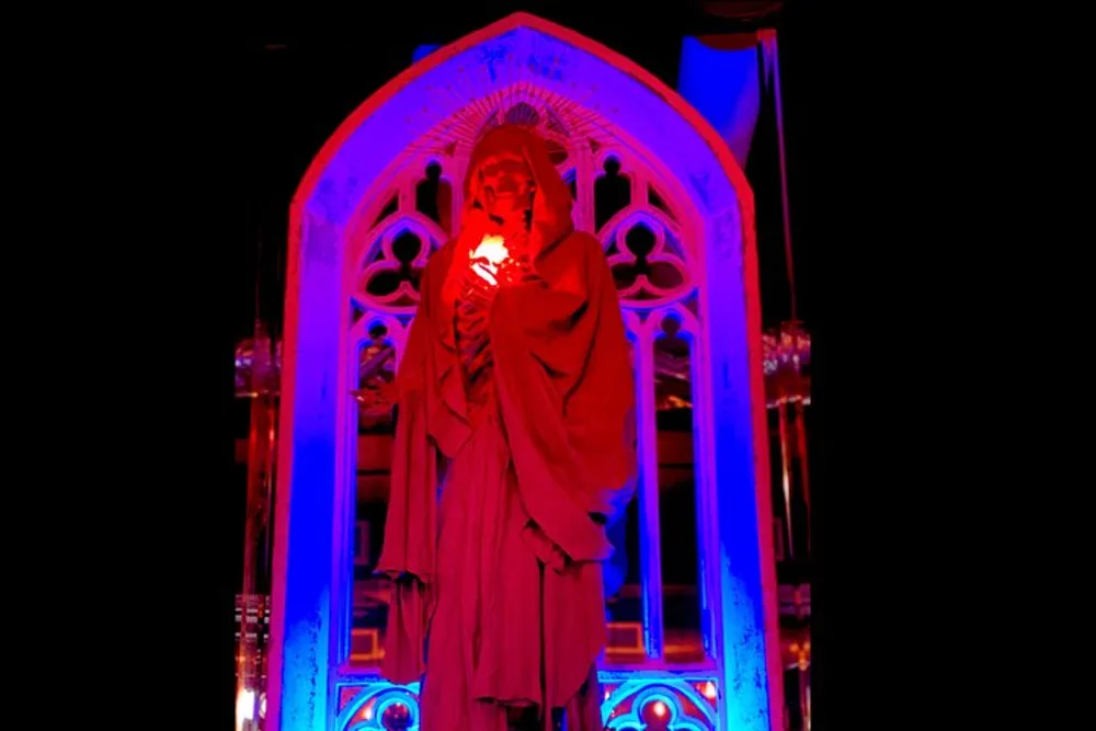 A statue stands within a gothic arch bathed in ominous red and blue lighting