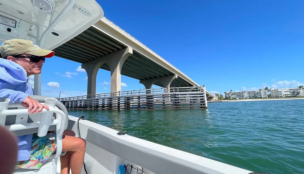 A person is sitting on a boat gazing toward a bridge over a body of water under a blue sky