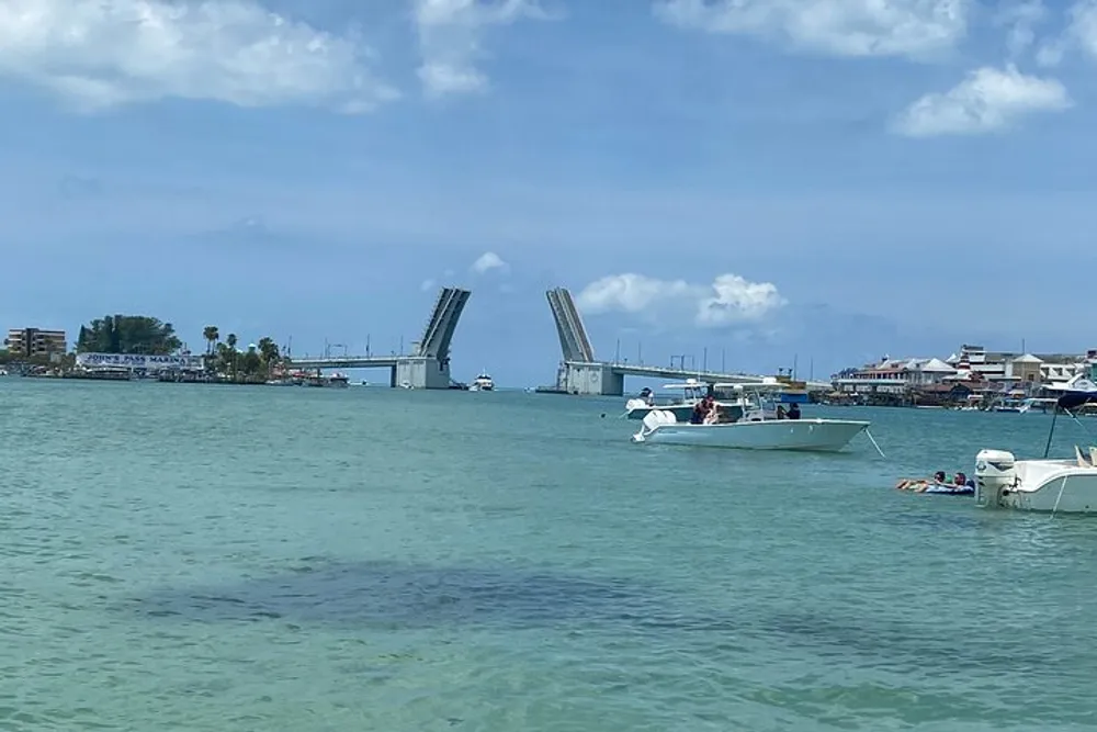 The image shows a sunny day with a raised drawbridge in the background allowing boat traffic to pass through in turquoise waters with several boats and a few people enjoying the day