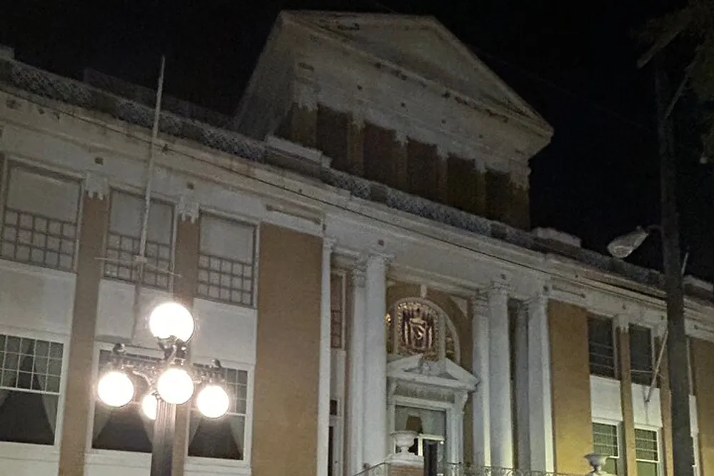 The image shows a stately building at night with white columns and a lit streetlamp in the foreground