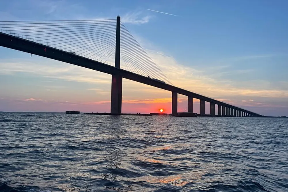 A cable-stayed bridge stretches across a body of water under a sunset sky