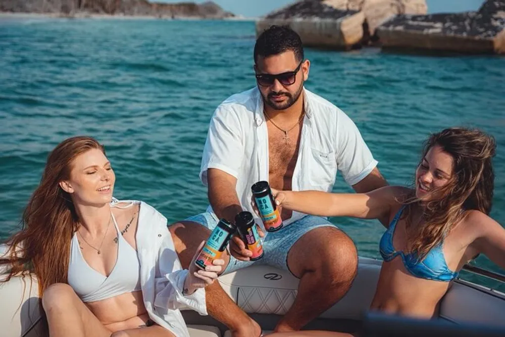 Three people are enjoying a sunny day on a boat while toasting with canned beverages
