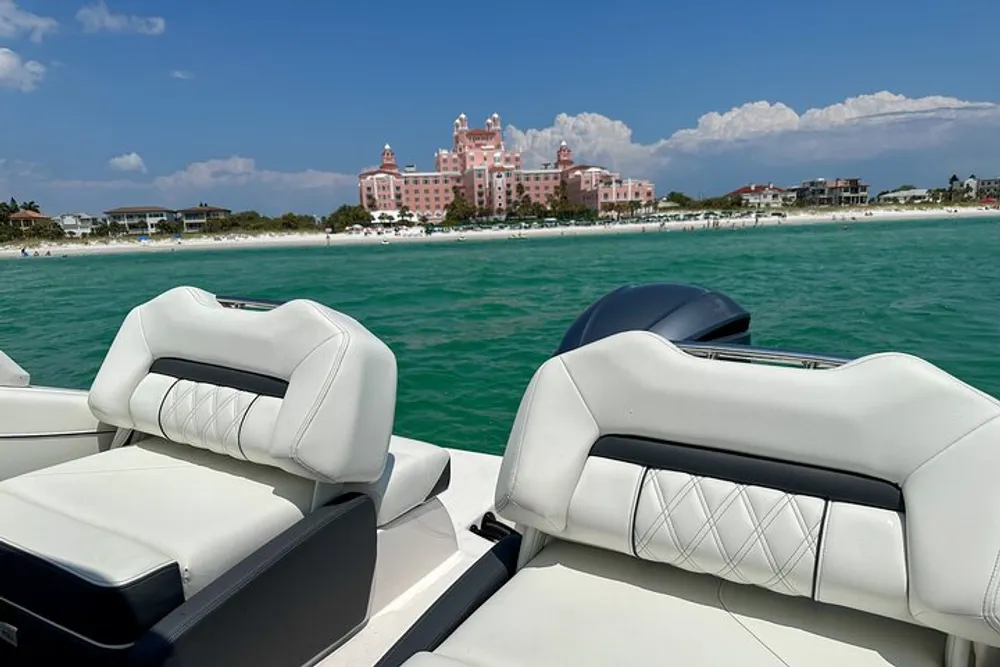 The image shows the view from a boat looking towards a grand pink building by the shoreline under a bright blue sky