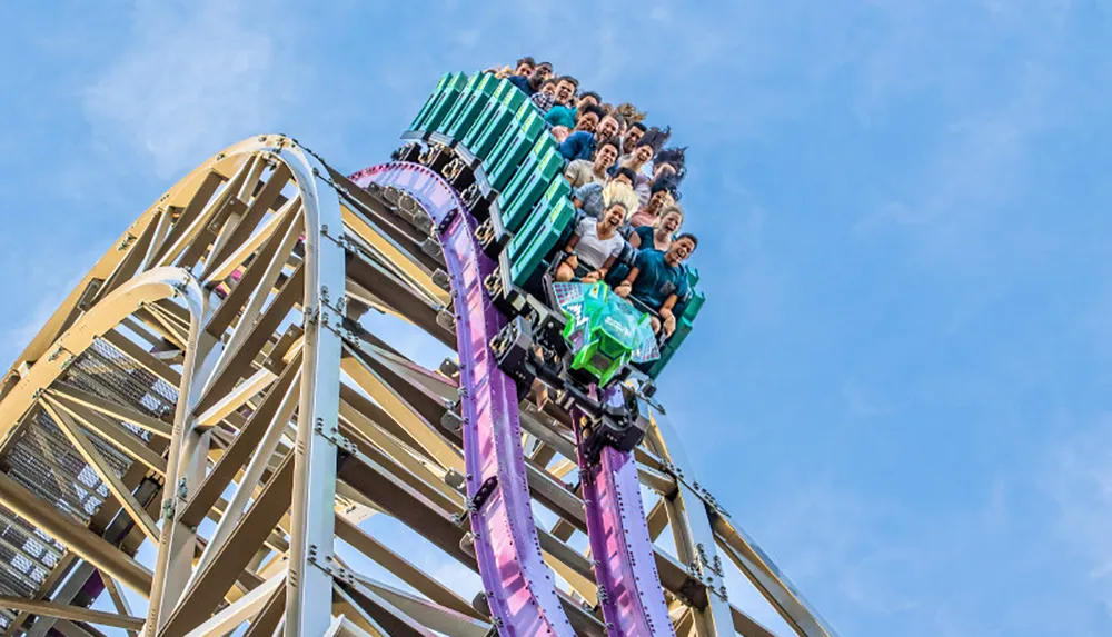 Thrilled passengers are descending a steep drop on a colorful roller coaster against a clear blue sky