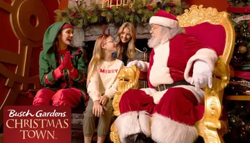 A group of people wearing festive Christmas attire is happily interacting with a person in a snowman costume at Busch Gardens' Christmas Town event.