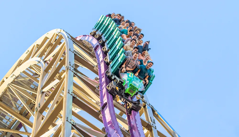 A large group of people are excitedly riding a roller coaster as it plunges down a steep descent under a clear blue sky
