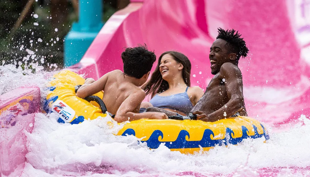 Three people are laughing and enjoying a thrilling ride down a colorful water slide on a shared inflatable raft