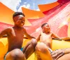 Two joyful children are sliding down a colorful water slide on a sunny day