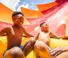 Two joyful children are sliding down a colorful water slide on a sunny day