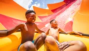 Two joyful children are sliding down a colorful water slide on a sunny day.