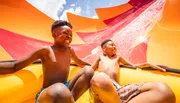 Two joyful children are sliding down a colorful water slide on a sunny day.