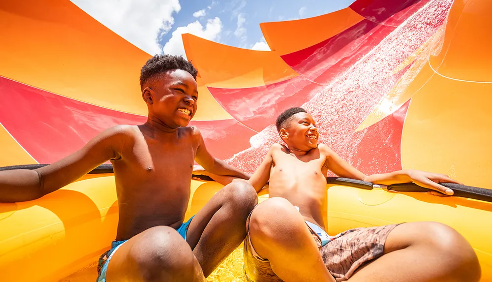 Two joyful children are sliding down a colorful water slide on a sunny day