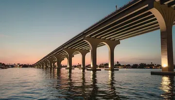 A long bridge spans across tranquil water with a backdrop of a twilight sky.