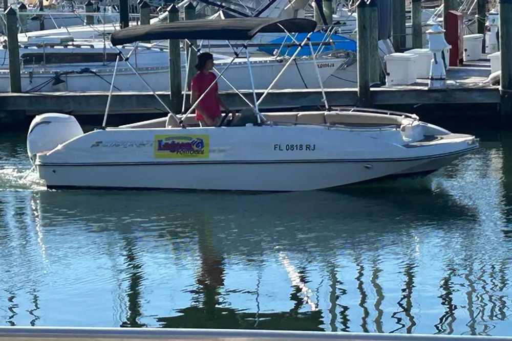 A person is standing on a dock next to a white speedboat named Latitude Adjustment which is moored in a marina with other boats