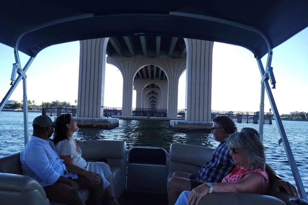 A group of people is sitting on a boat enjoying a scenic view as they pass under a large bridge with distinctive arches