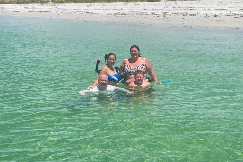 Four people are smiling while enjoying a sunny day wading in clear shallow water at a beach