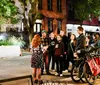 A group of people gather around a lantern at night intently listening to a hooded tour guide wearing a US Ghost Adventures jacket seemingly part of a ghost tour