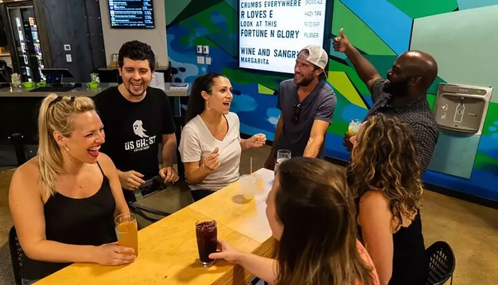 A group of people are sharing a lively moment at a bar with one person enthusiastically pointing to a menu board while the others laugh and enjoy their drinks