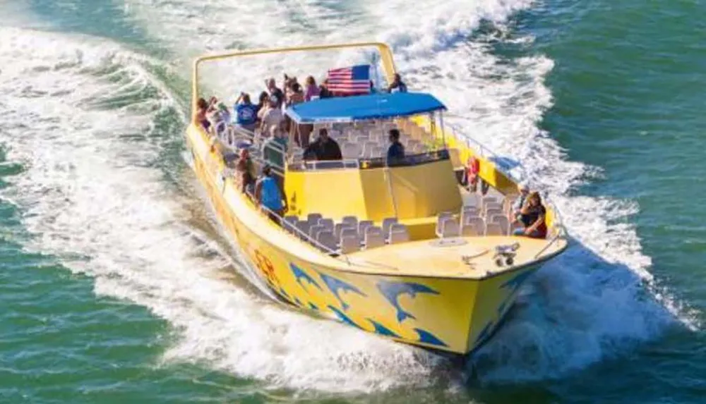 A group of passengers are enjoying a ride on a vibrant yellow tour boat as it speeds across the water creating a wake behind it