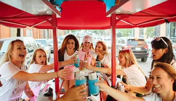 A group of joyful friends are toasting with drinks while enjoying a ride on a pedal pub.