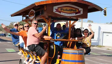 A group of people is joyfully riding a pedal-powered bar on wheels down a street.