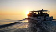 A boat full of passengers is cruising on calm waters at sunset, creating a tranquil and beautiful scene.