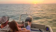 Two people are enjoying a sunset from the back of a boat on the water.