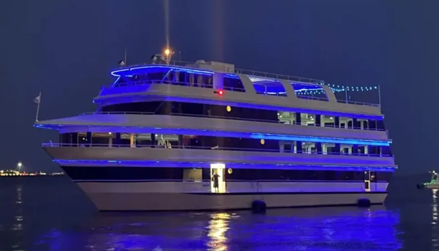 A large yacht illuminated with blue lights is seen on the water at night.