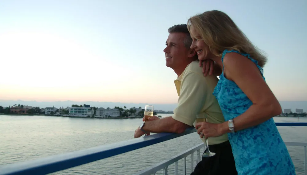 A couple is enjoying a romantic moment with glasses of wine on a boat overlooking the waterfront at dusk