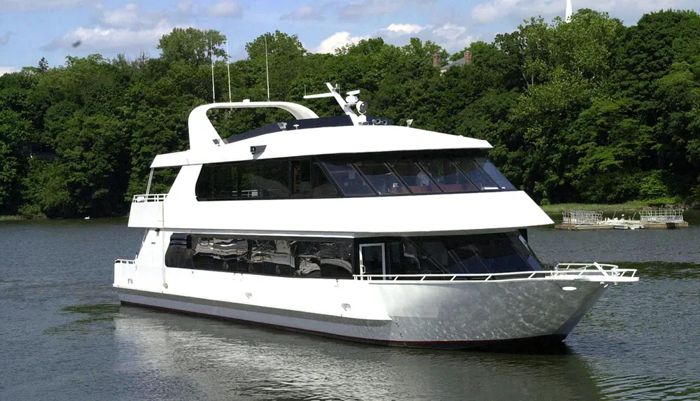 A white luxury yacht is cruising on a calm river with a backdrop of lush greenery