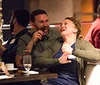 Two people are sharing a jovial moment with laughter at a social gathering