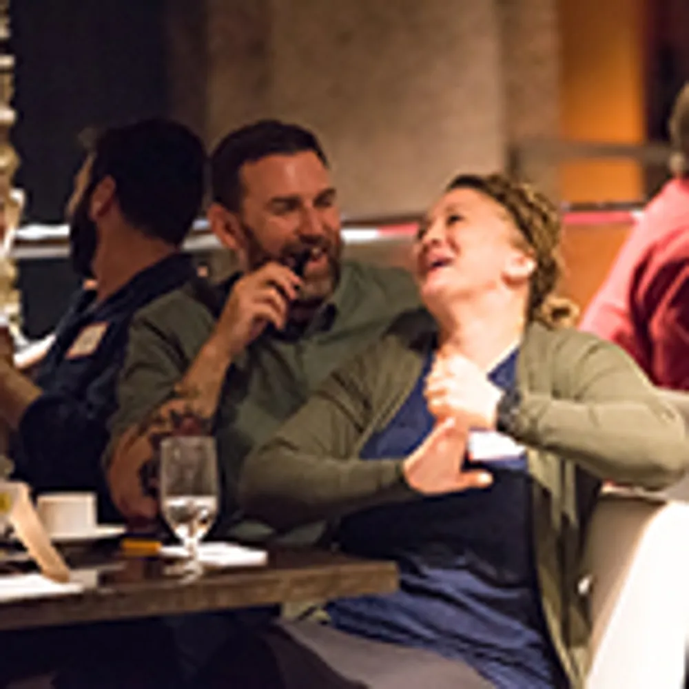 Two people are sitting at a table sharing a laugh in a lively indoor setting