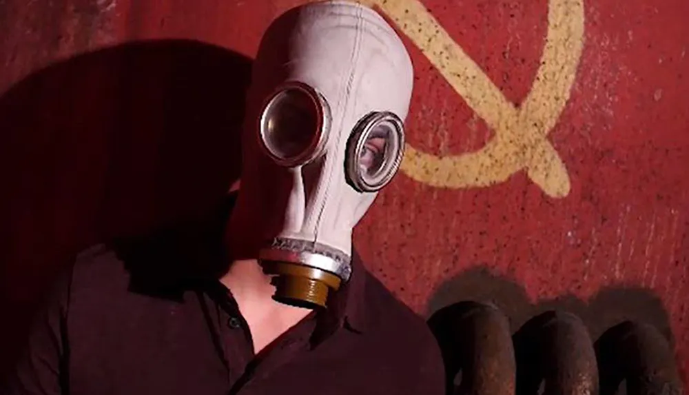 A person is wearing a vintage gas mask in front of a wall with a graffiti symbol