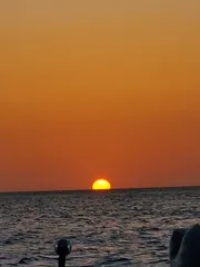 The image captures a tranquil sunset with the sun half-dipped below the horizon over a calm sea, emitting a warm orange glow that fills the sky.