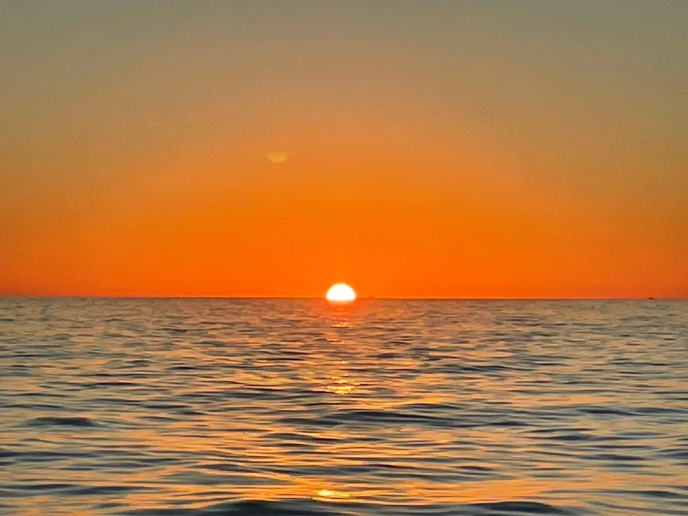 The image depicts a serene sunset over a calm ocean casting a vibrant orange glow across the sky and water