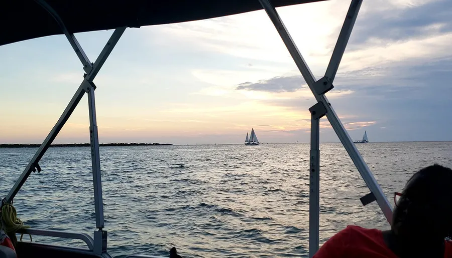 This image captures a tranquil evening on the water, featuring the view from a boat as passengers observe sailboats on the horizon under a softly colored sunset sky.