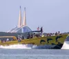 A large yellow boat with dolphin graphics is speeding through the water with passengers on board with a bridge in the distant background