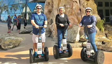 Three people are standing side by side outdoors, each on a Segway, with helmets on for safety, smiling for the camera.
