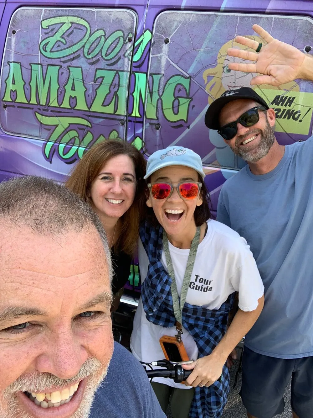 A group of four people is taking a joyful selfie with a smiling man in the foreground and a colorful van with the text DOOM AMAZING in the background