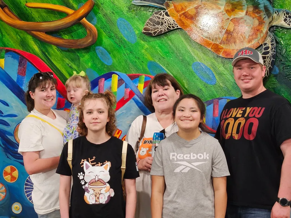 A group of six individuals likely a family is posing for a photo with a vibrant underwater-themed mural featuring a large turtle in the background