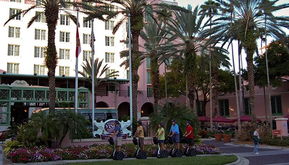 A group of people are riding Segways in front of a palm-lined pink building facade