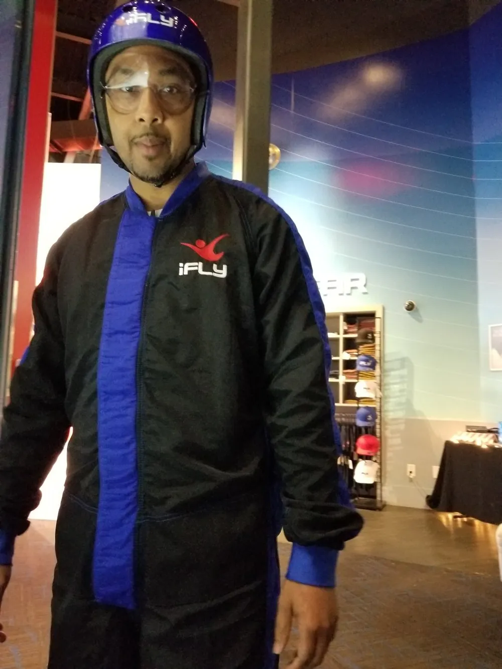 A person is wearing a blue helmet and an iFLY branded flight suit possibly preparing for or having just experienced an indoor skydiving session