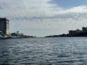 The image shows a waterfront view with buildings on the left, a clear horizon, and a partly cloudy sky above a broad expanse of water.